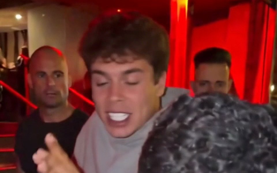 Young man in a gray hoodie rapping before a crowd at night