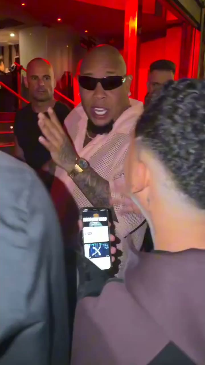 The original street freestyle at night: the rapper in front of a red-lit doorway, a man with a portable speaker in the foreground