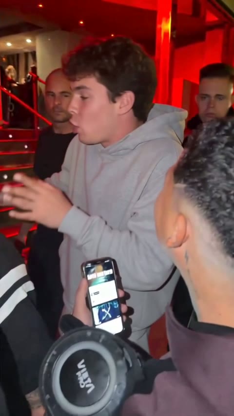 Young man with curly brown hair and a gray hoodie rapping in the crowd at night