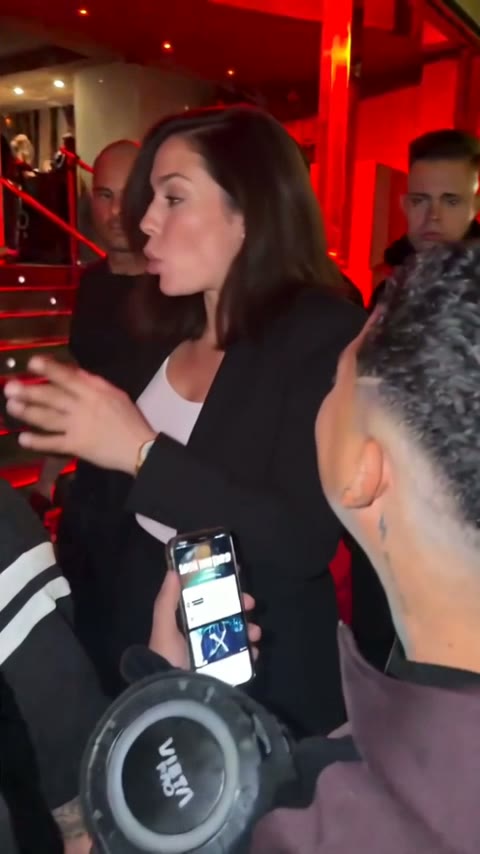 Woman in her thirties, dark hair, black blazer, turning toward the phone